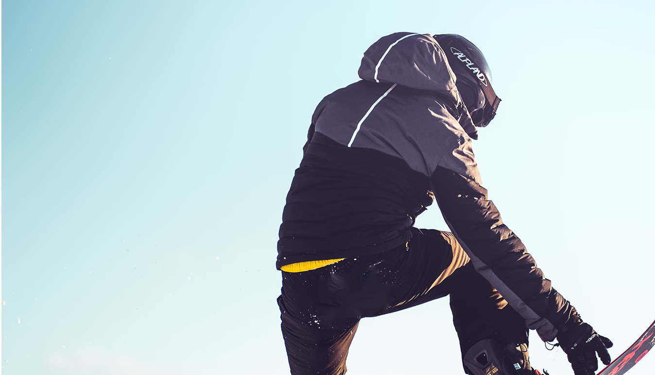 A person wearing a winter jacket with a hood, riding a bicycle. The jacket is primarily black with some gray and yellow details.